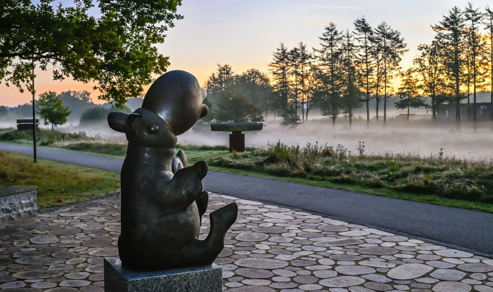 Bronze bear sculpture by a path in Billund Sculpture Park on a misty morning